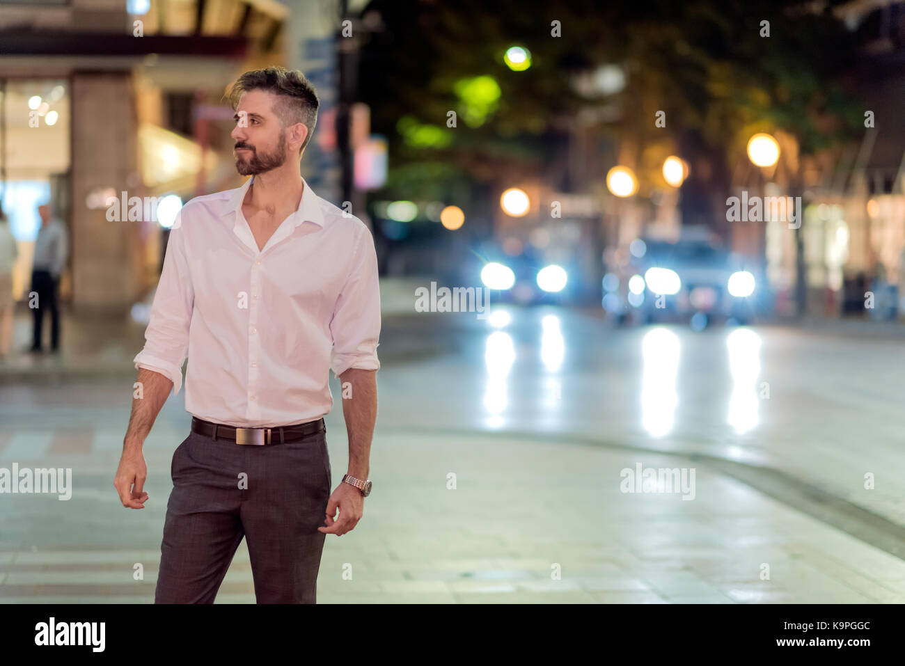 Handsome caucasian male professional photographed on the street at night standing on corner of intersection with background traffic. Stock Photo