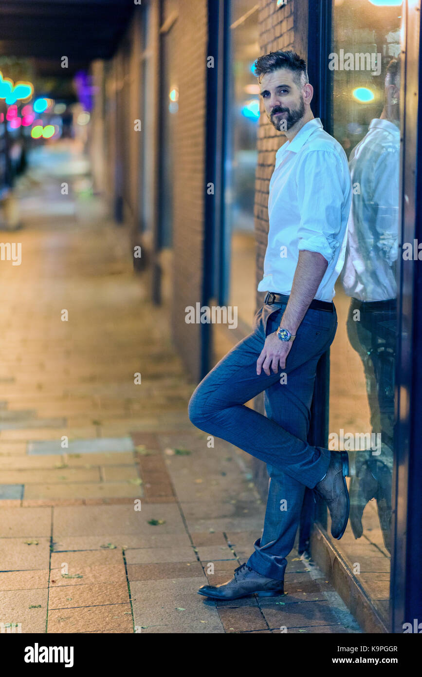 Handsome caucasian male professional photographed on the street at night standing against a shop window. Stock Photo