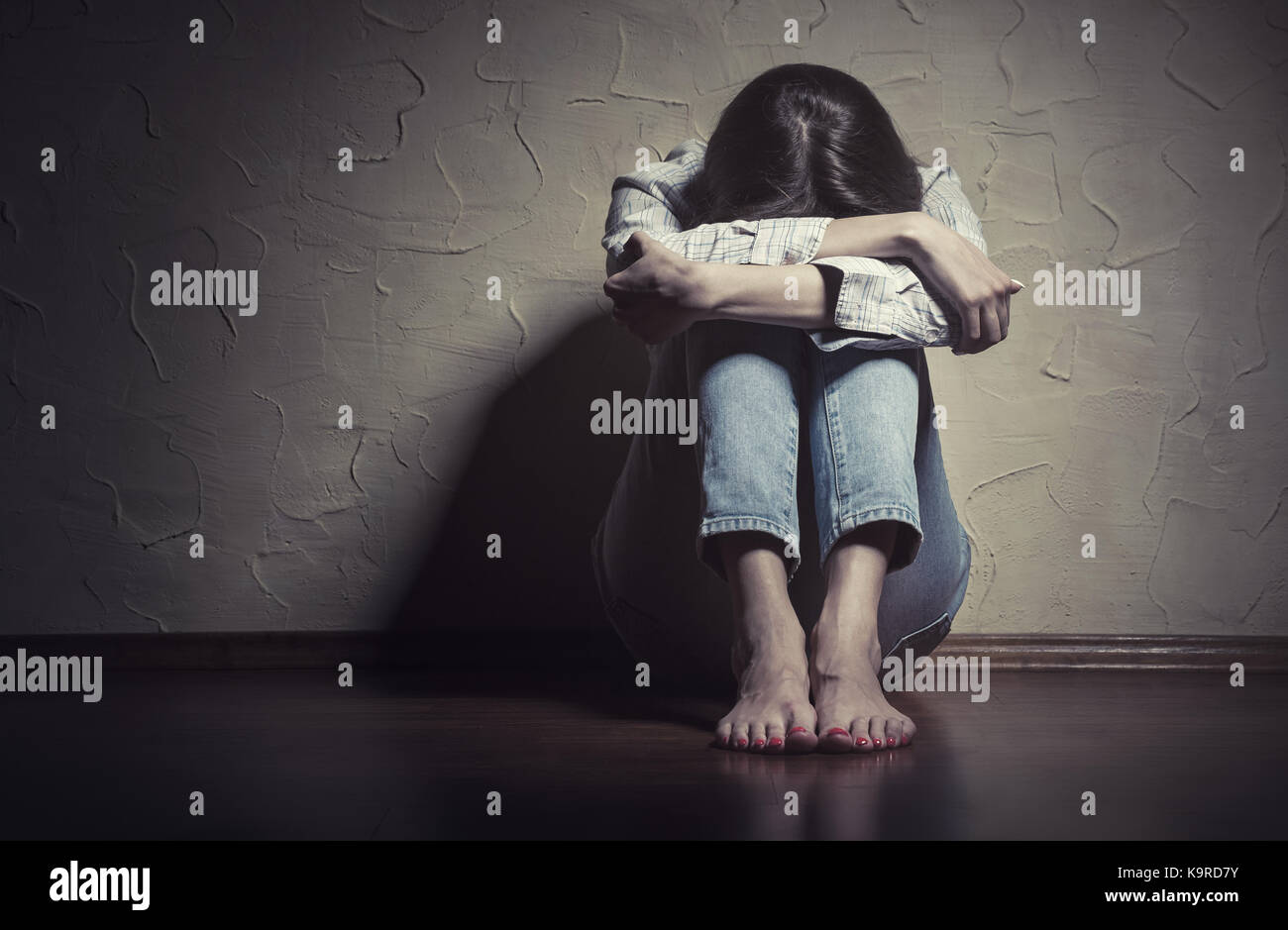 Young sad woman sitting alone on the floor in an empty room Stock Photo