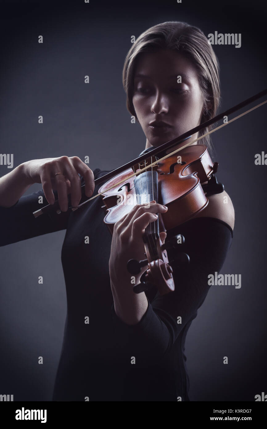 Beautiful young woman playing the violin against a dark background Stock Photo