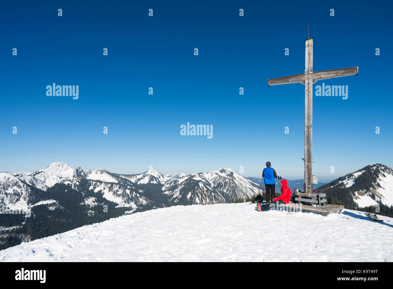 Backcountry skiers at the latin cross of the summit of Mount Rosskopf looking at the panorama of the snowy Bavarian Alps in spring, Bavaria, Germany Stock Photo