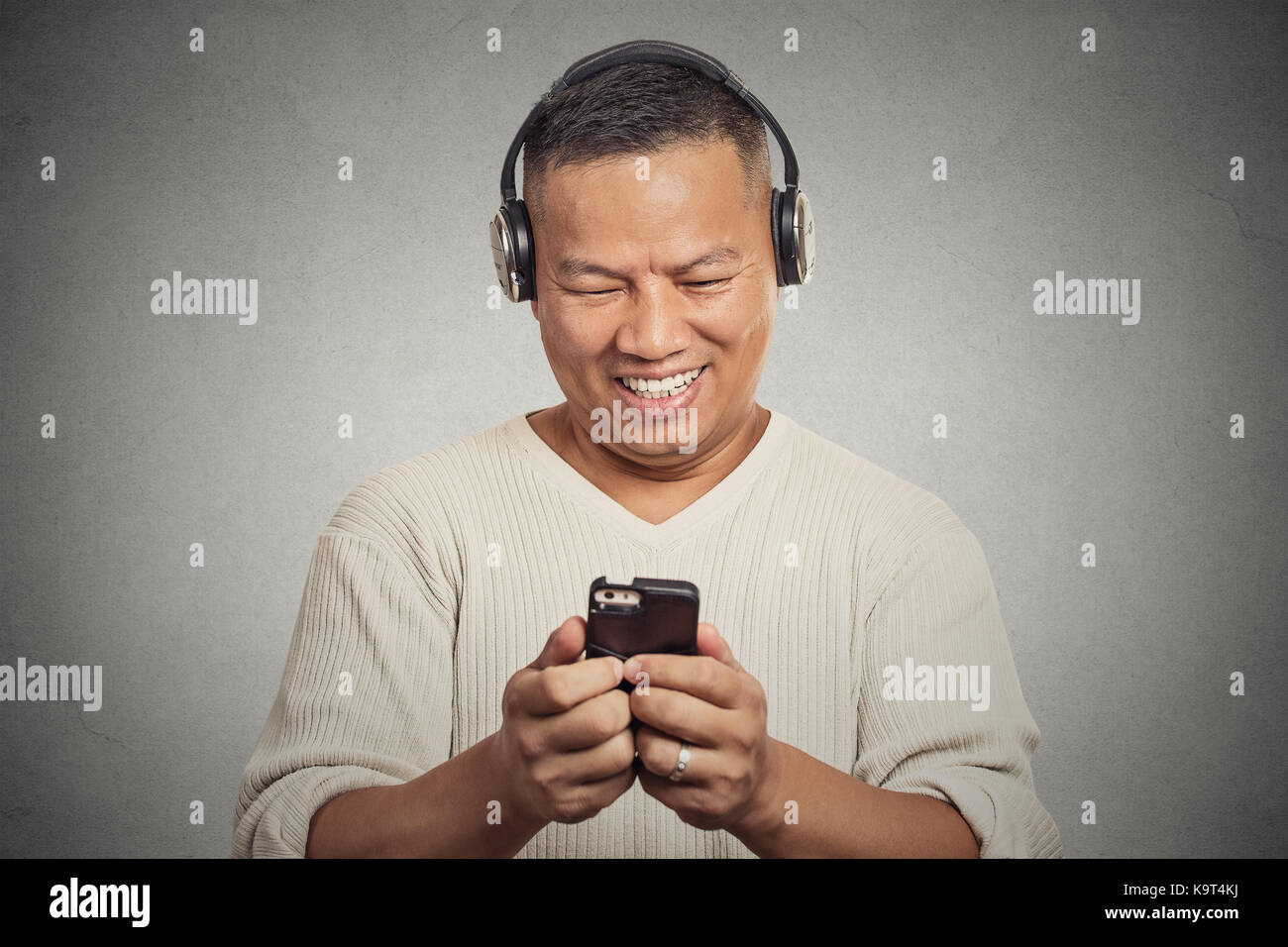 Portrait casual smiling young man listening music on cell phone isolated on grey wall background. Positive facial expression emotion. Technology leisu Stock Photo