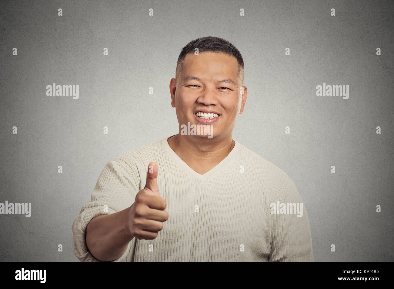 Closeup portrait happy handsome young smiling man employee giving thumbs up sign gesture at camera isolated grey wall background. Positive human emoti Stock Photo