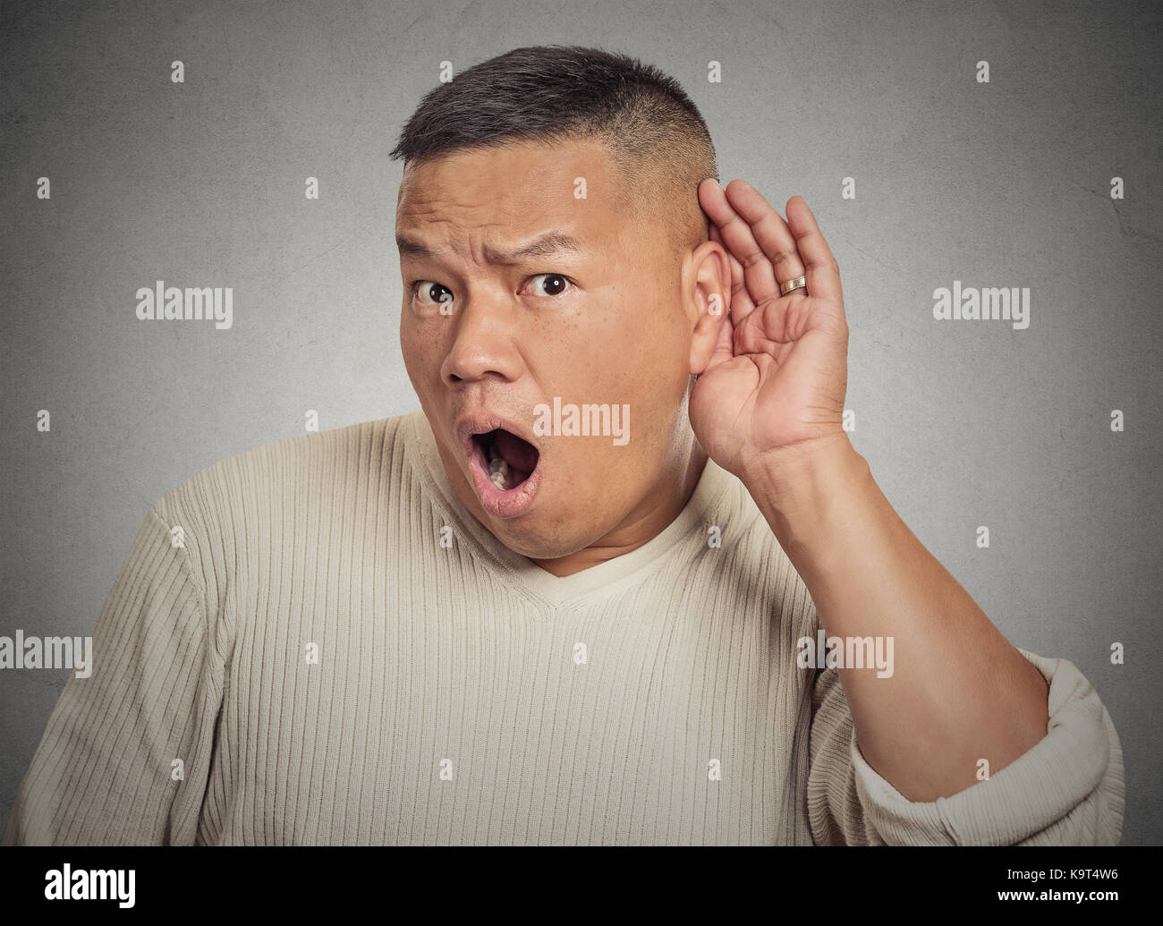 Closeup portrait of guy listening in on a conversation and seeming shocked by what he hears isolated on grey background with copy space Stock Photo