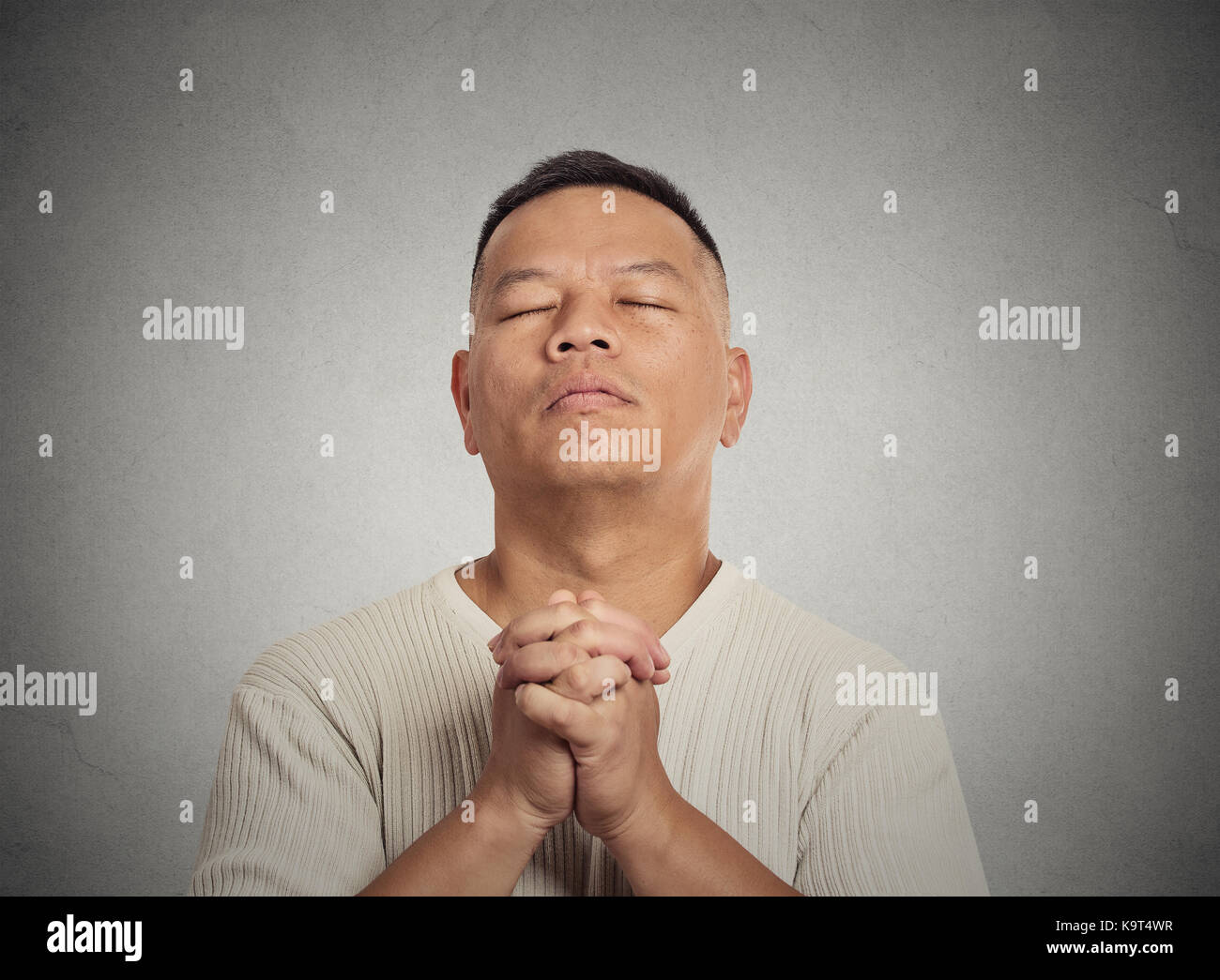 Closeup portrait middle aged man eyes closed praying looking up hoping for best asking for forgiveness, miracle isolated grey wall background. Human e Stock Photo