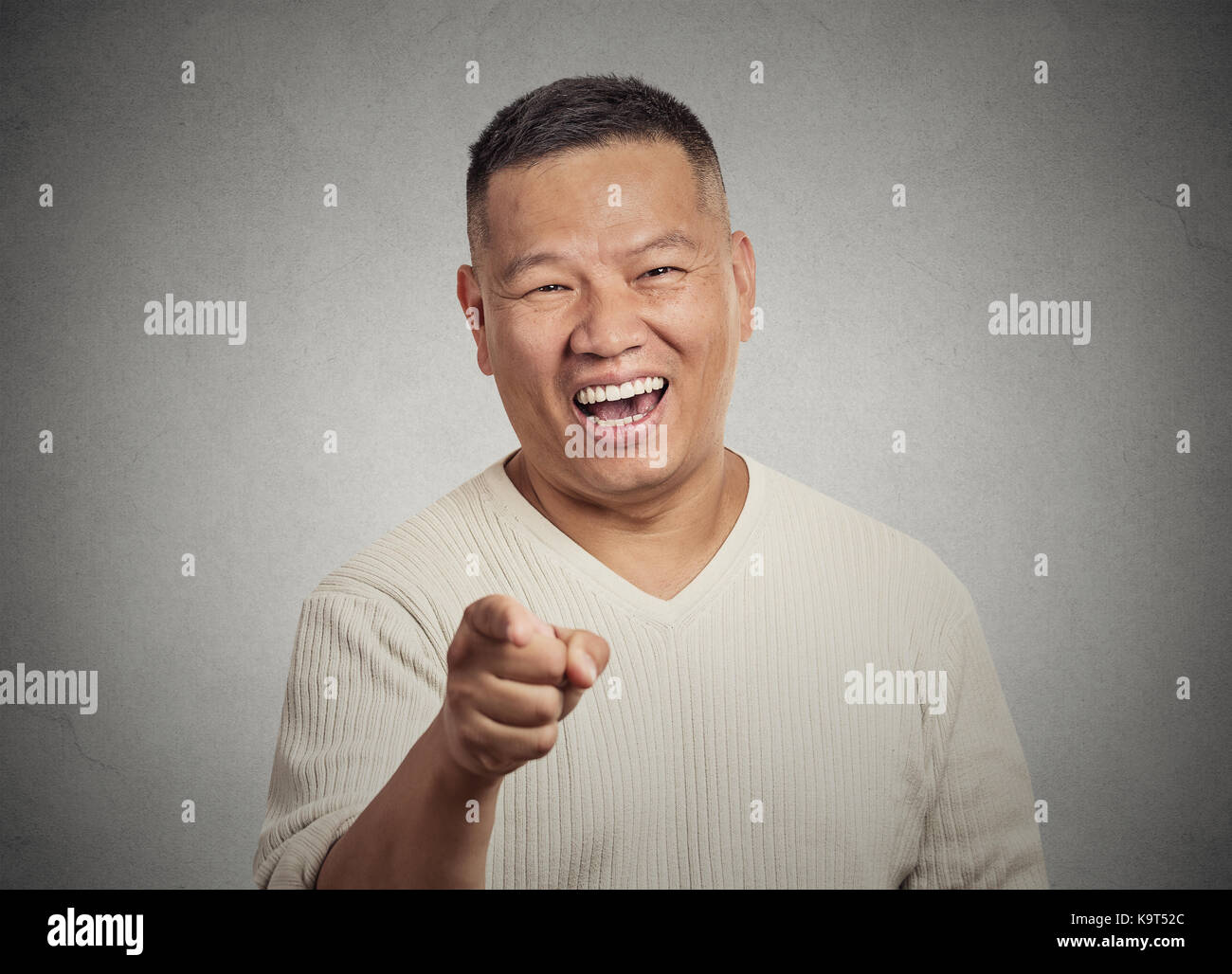 Closeup portrait young man, laughing, pointing with finger at someone something isolated grey wall background. Positive human face expressions, emotio Stock Photo