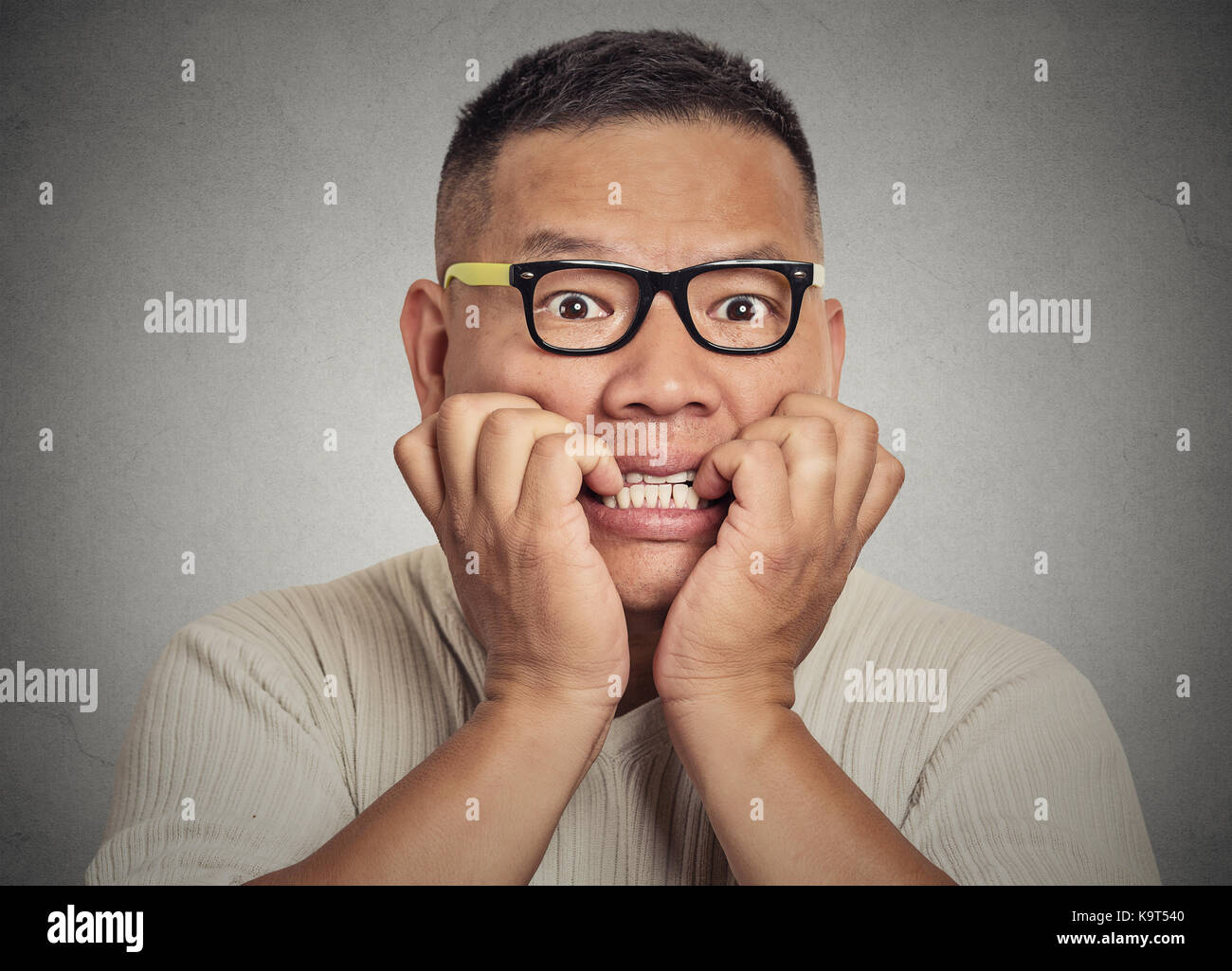 Closeup portrait headshot nerdy young guy with glasses biting his nails looking at you with craving for something or anxious isolated on grey wall bac Stock Photo