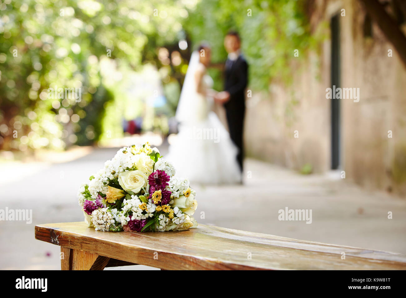 bouquet on wooden bench with bride and groom in the background, focus on the flowers. Stock Photo