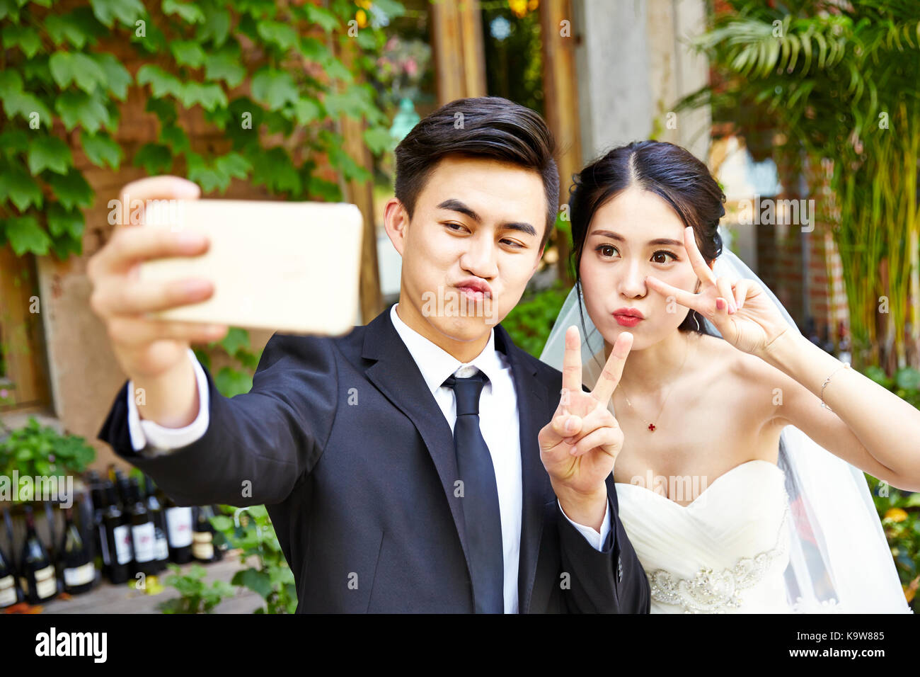 happy young asian bride and groom making a face while taking a selfie using cellphone. Stock Photo