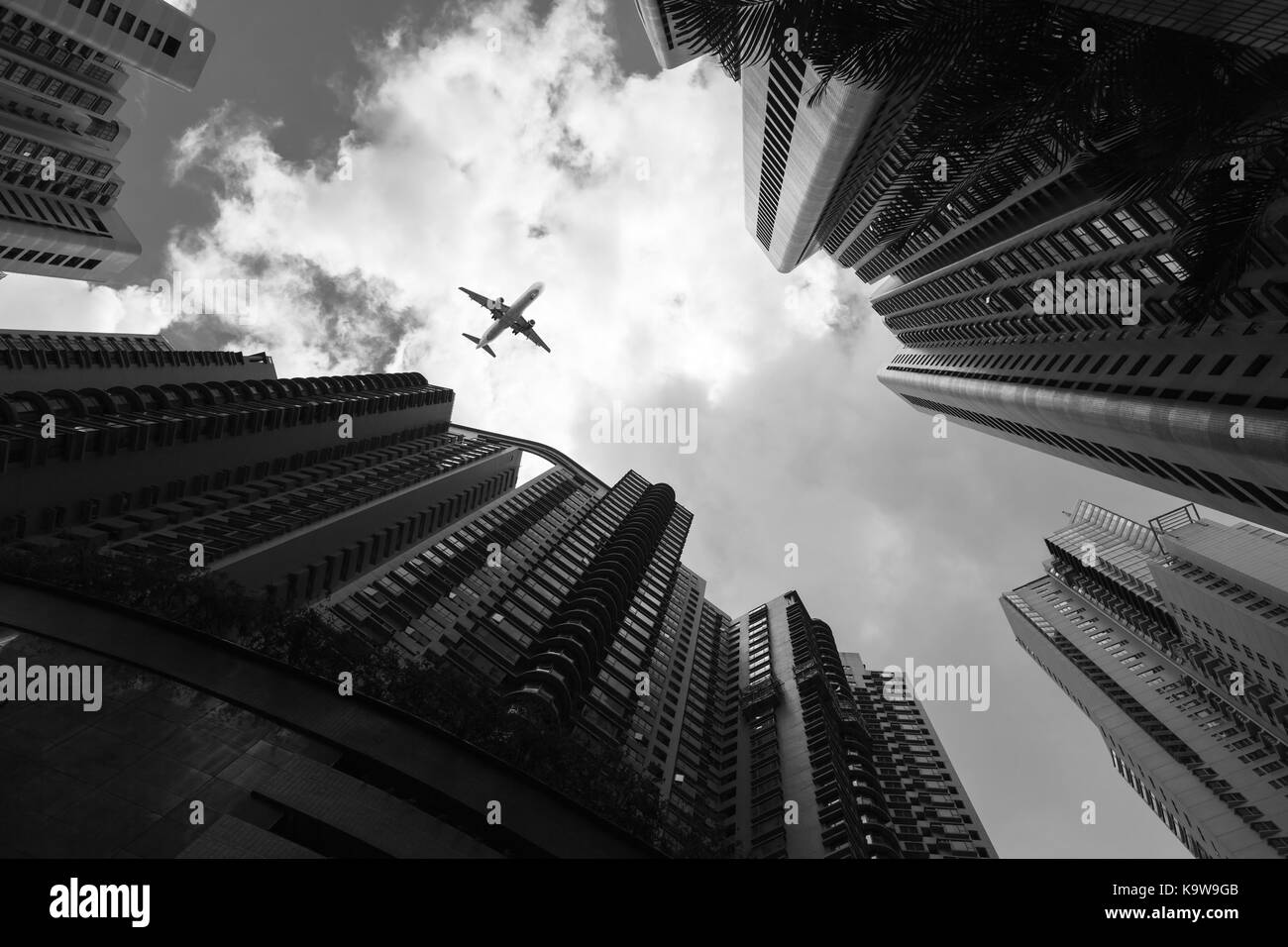 Urban skyline with passenger plane flying over business skyscrapers, high-rise office buildings of Hong Kong, black and white Stock Photo