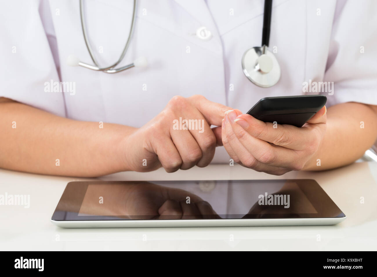 Close-up Of Doctor Using Mobile Phone With Digital Tablet At Desk Stock Photo