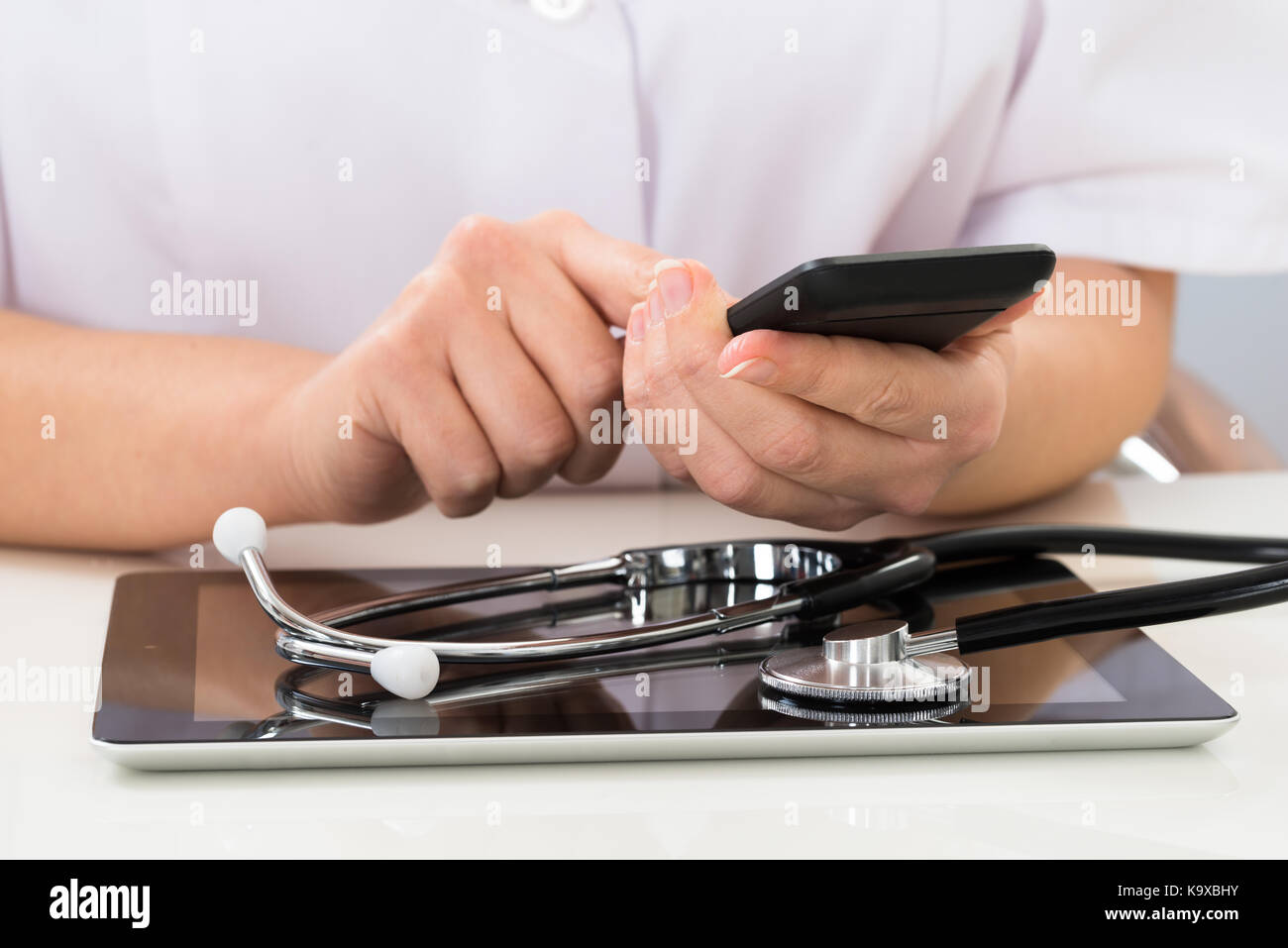 Close-up Of Doctor Using Mobile Phone With Digital Tablet At Desk Stock Photo