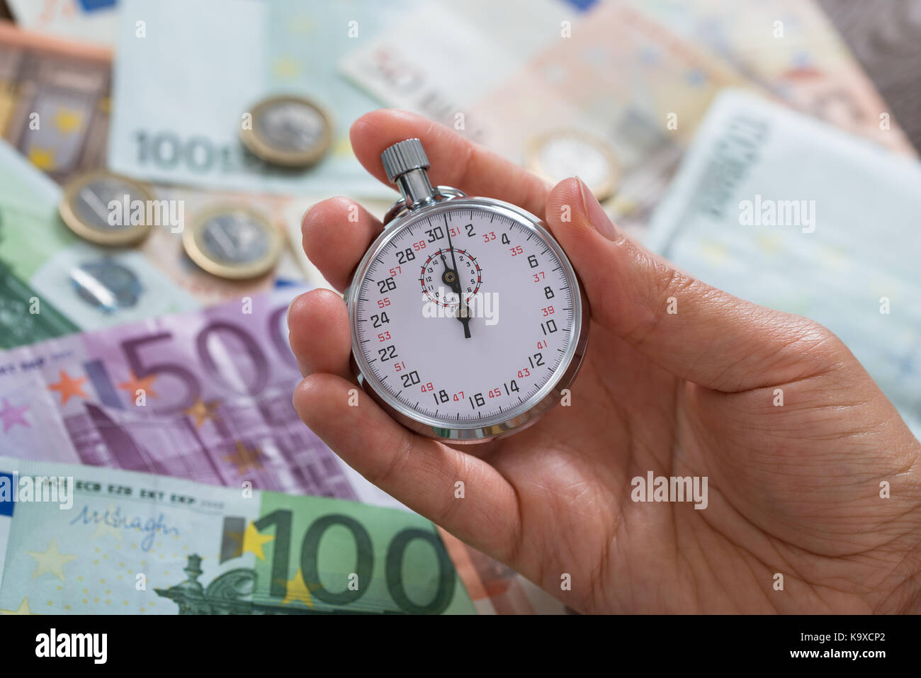 Close-up Of Person Hands Holding Stopwatch Over Money Background Stock Photo