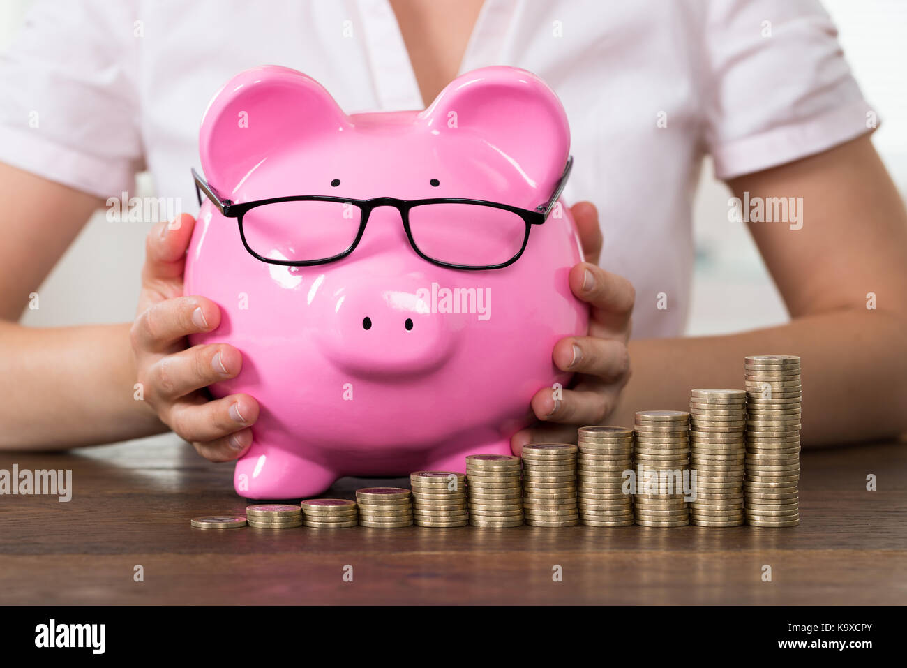 Close-up Of Businesswoman With Piggybank And Stack Of Coins At Desk Stock Photo