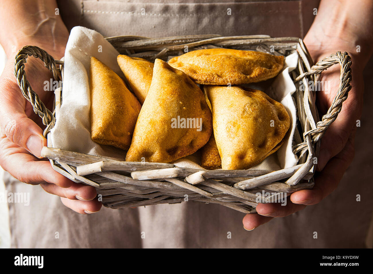 Young woman holding in hands wicker basket with freshly baked empanadas turnover pies with vegetables cheese in tomato sauce. Knfolk style. Cozy authe Stock Photo
