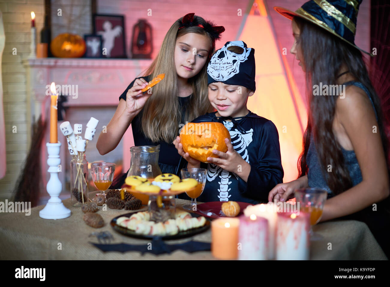 Curious little friends interested in Halloween traditions opening carved pumpkin lantern and looking what is inside while having fun at party and eati Stock Photo