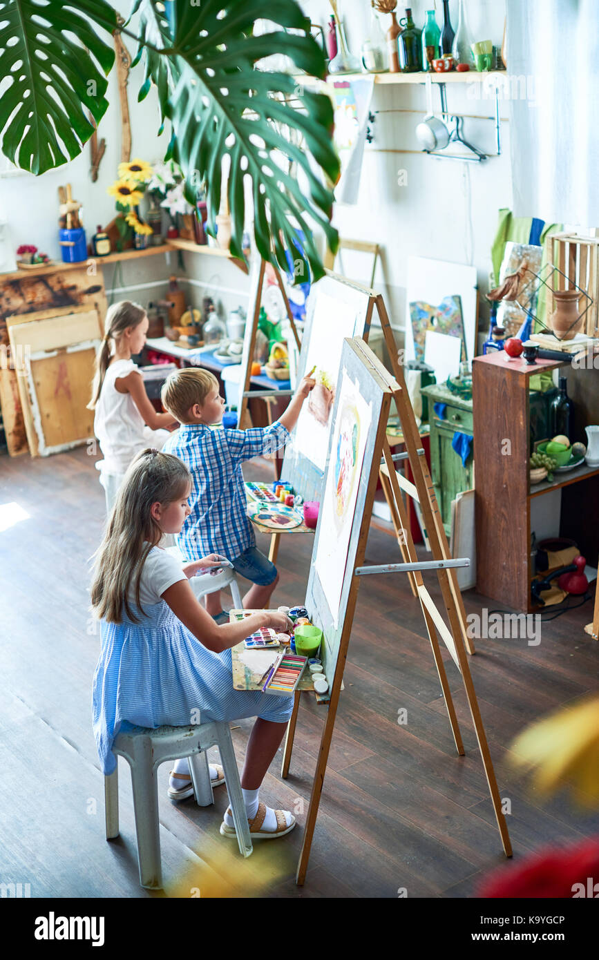 High angle portrait of three children painting on easels during art ...