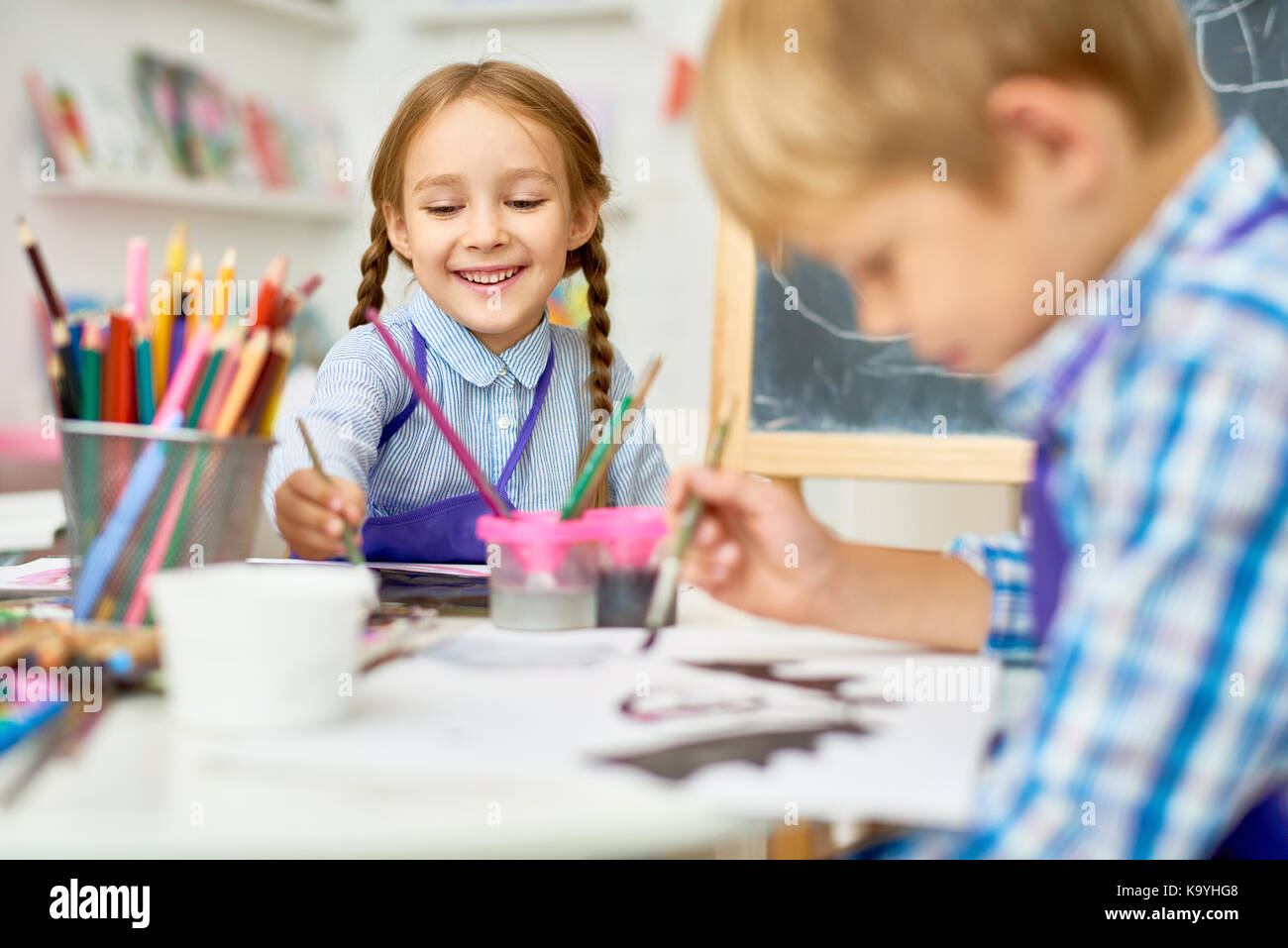 Portrait of adorable little girl smiling happily while enjoying art and craft lesson in pre school working together with boy Stock Photo
