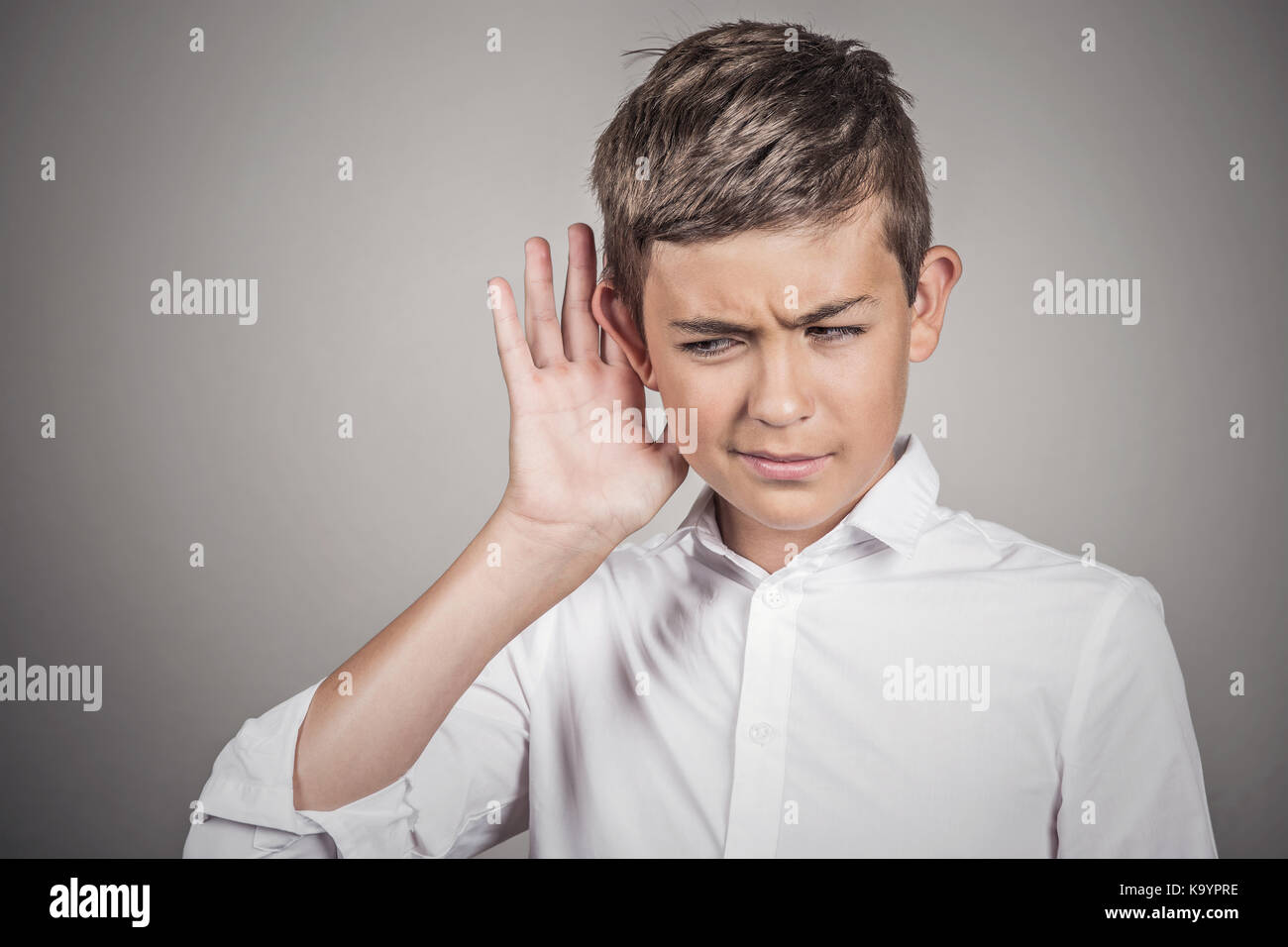 Closeup portrait handsome guy secretly listening in on private conversation, hand to ear gesture, privacy violation concept isolated grey wall backgro Stock Photo