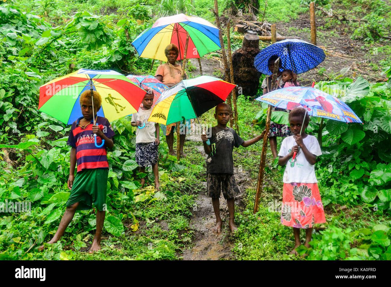 Native women with children with colourful umbrellas in the rain in the village of Rangsuksuk, island of Pentecost, Vanuatu Stock Photo