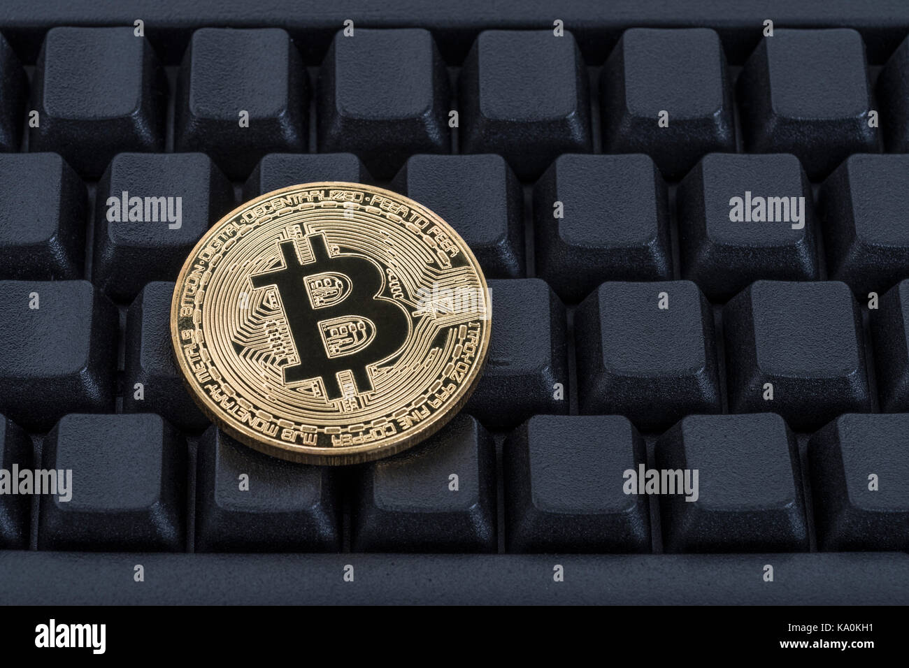 Gold coloured BitCoin / Bitcoin cryptocurrency token on a black Qwerty keyboard - metaphor for online transactions, Darkweb cybercrime, & e-commerce. Stock Photo