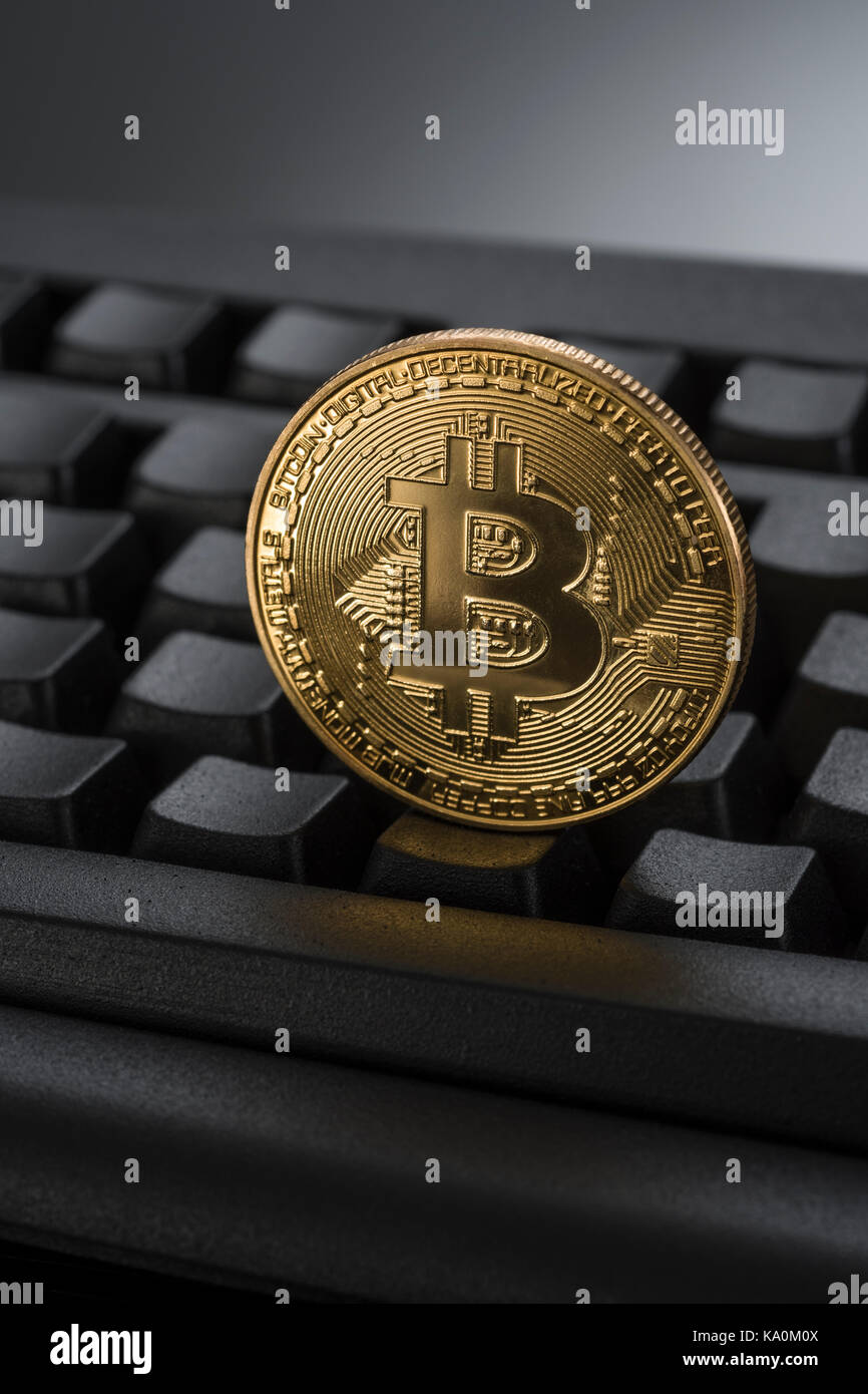 Gold coloured BitCoin / Bitcoin cryptocurrency token on a black Qwerty keyboard - metaphor for online transactions, Darkweb cybercrime, & e-commerce. Stock Photo