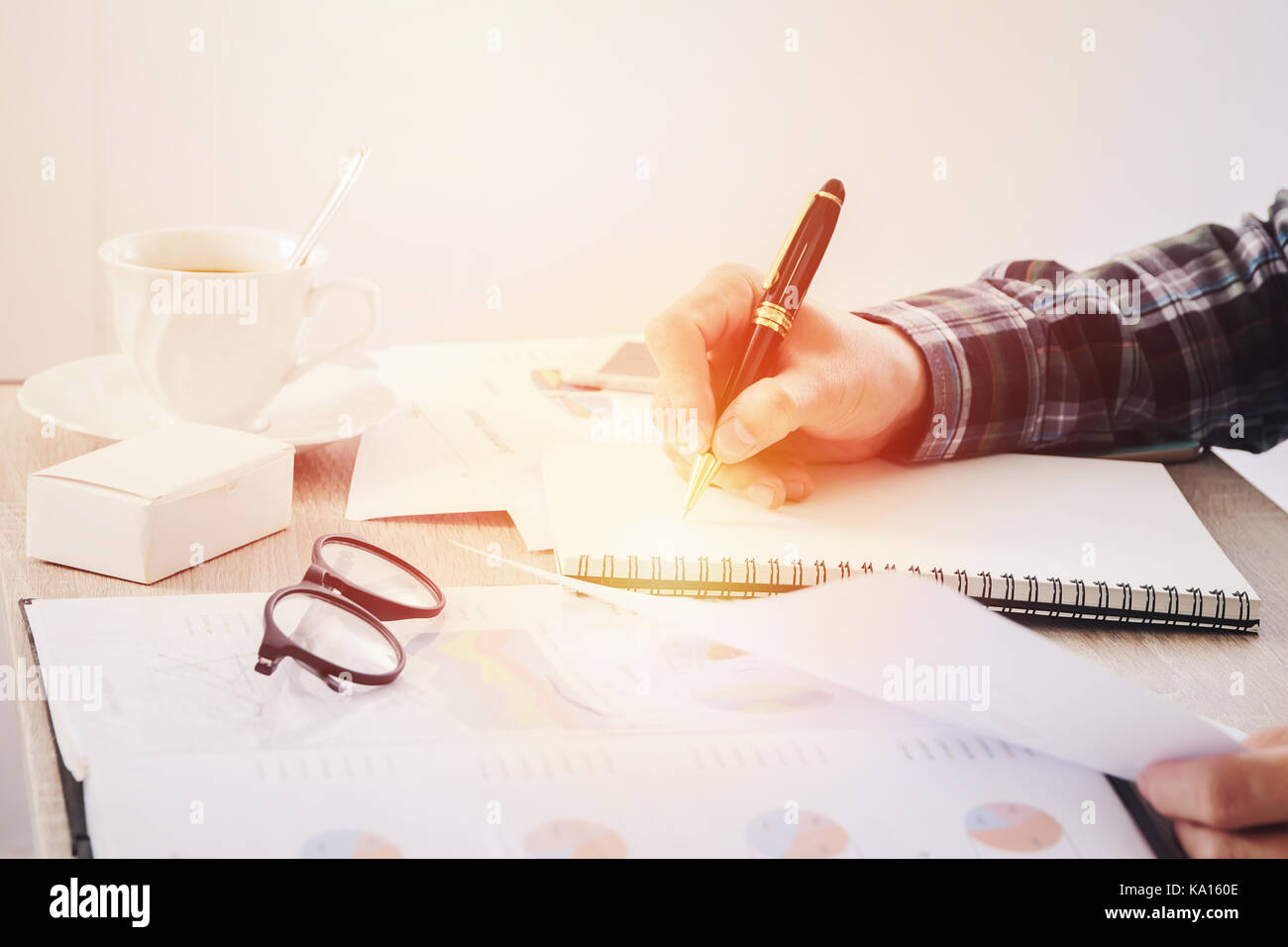 Hands of businessman writing something on notebook paper, and business finance report document blurred on table. Stock Photo