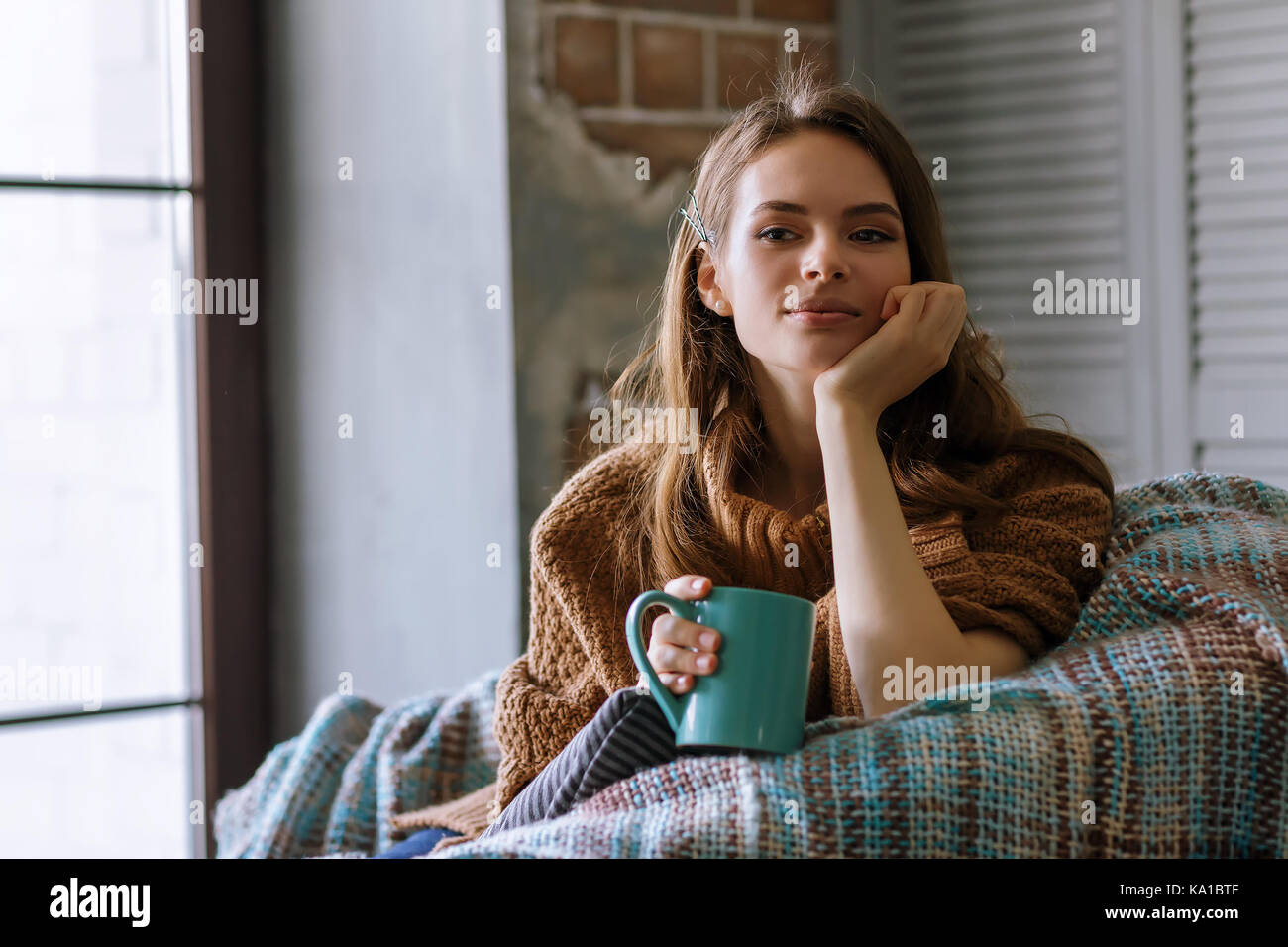 Photo in home atmosphere of young beautiful girl sitting in a chair with a mug of coffee Stock Photo