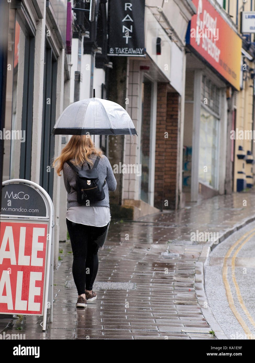 Lady walking up Bideford High Street in the rain carrying an umbrella Stock Photo