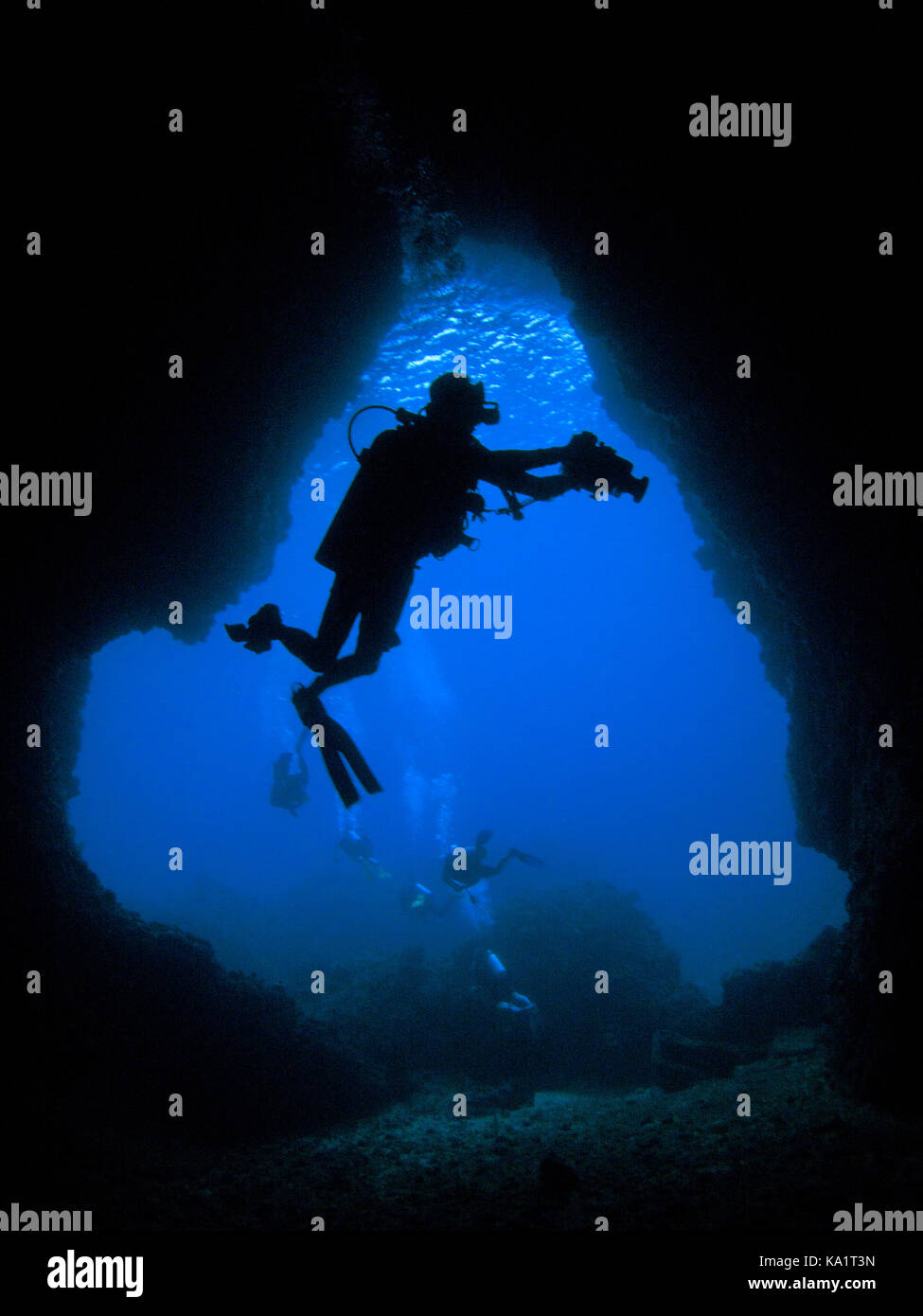 Scuba diver with video camera silhouetted in mouth of an underwater cave Stock Photo