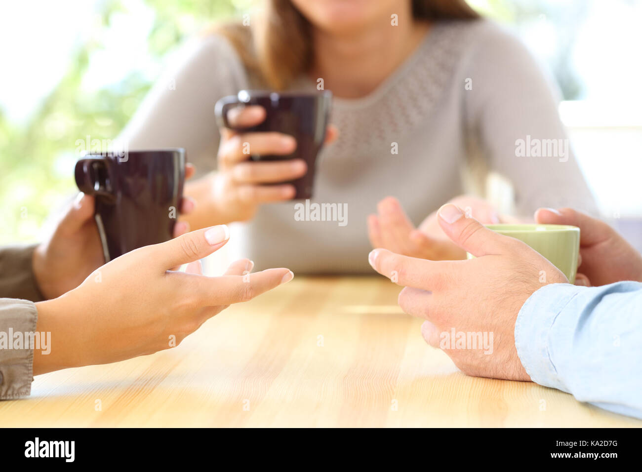 Close up of three friends hands talking and holding coffee cups sitting in a table in a bar or home Stock Photo