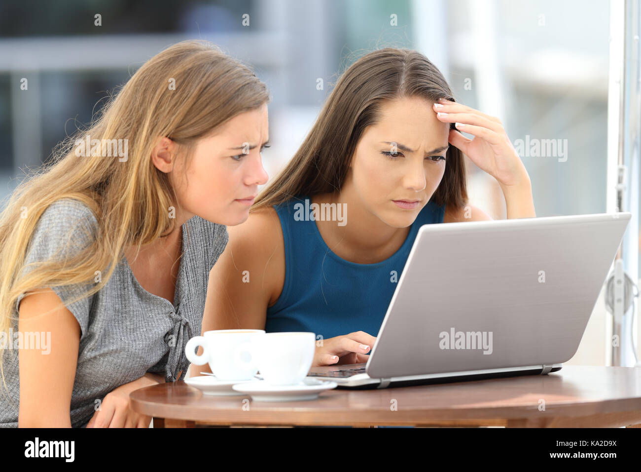 Two worried friends watching media content on line in a laptop sitting in a restaurant terrace Stock Photo