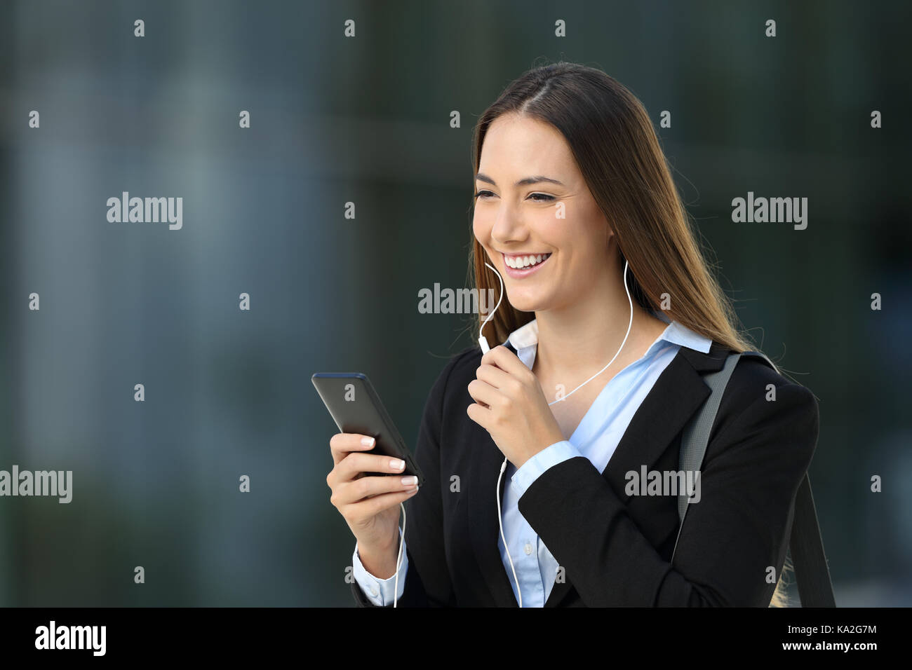 Happy executive talking with earphones during a phone call on the street with an office building in the background Stock Photo