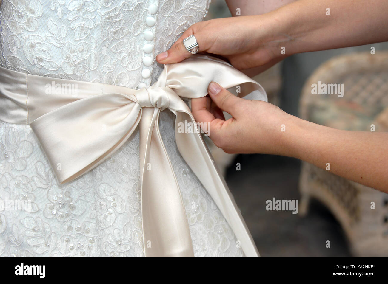Hands tie the satin bow of wedding gown. Closeup of female hands