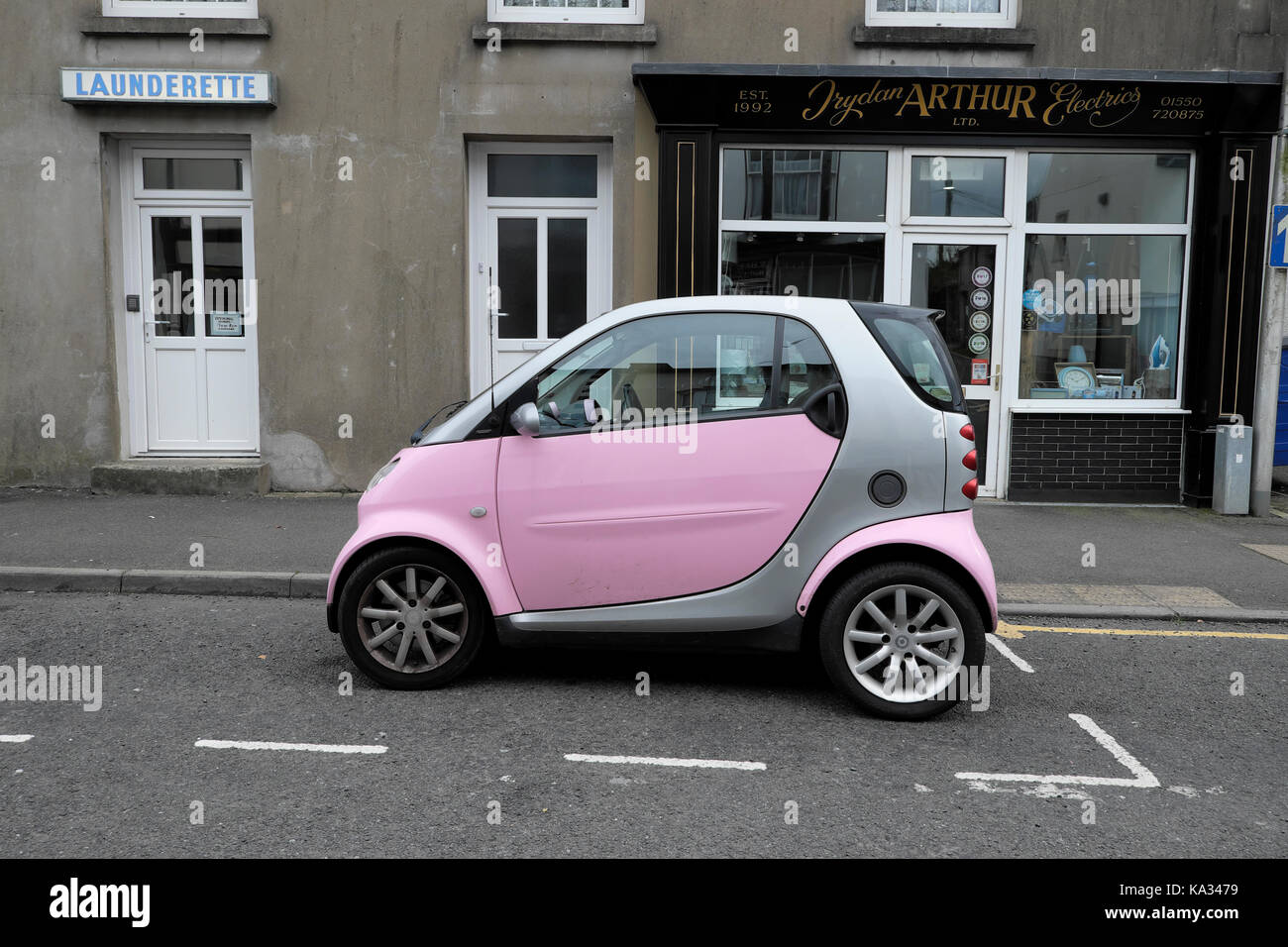 A pink and silver Smart Car parked in a parking space outside a laundrette in a Llandovery street Carmarthenshire, Wales, UK  KATHY DEWITT Stock Photo