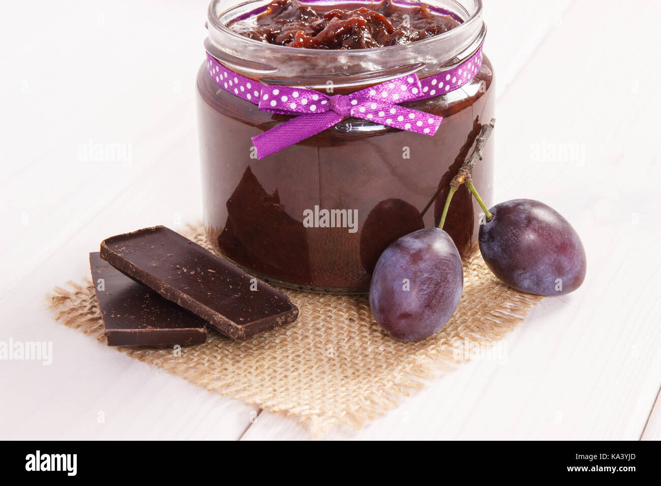 Fresh plum jam or marmalade in glass jar, ripe fruits and chocolate, concept of healthy sweet dessert Stock Photo