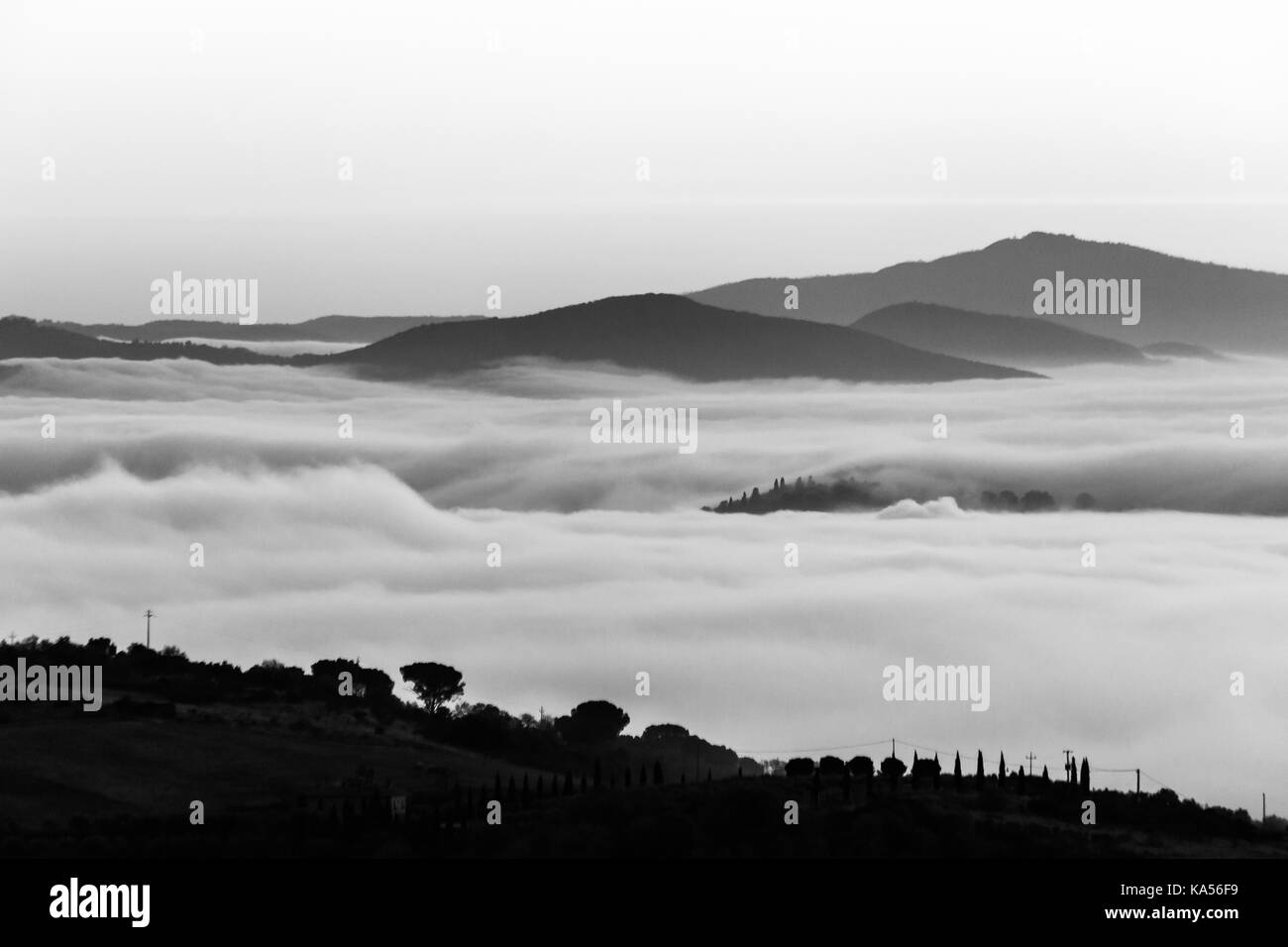 A valley filled by fog, with some hills and trees in the foreground and other hills and mountains in the foreground Stock Photo