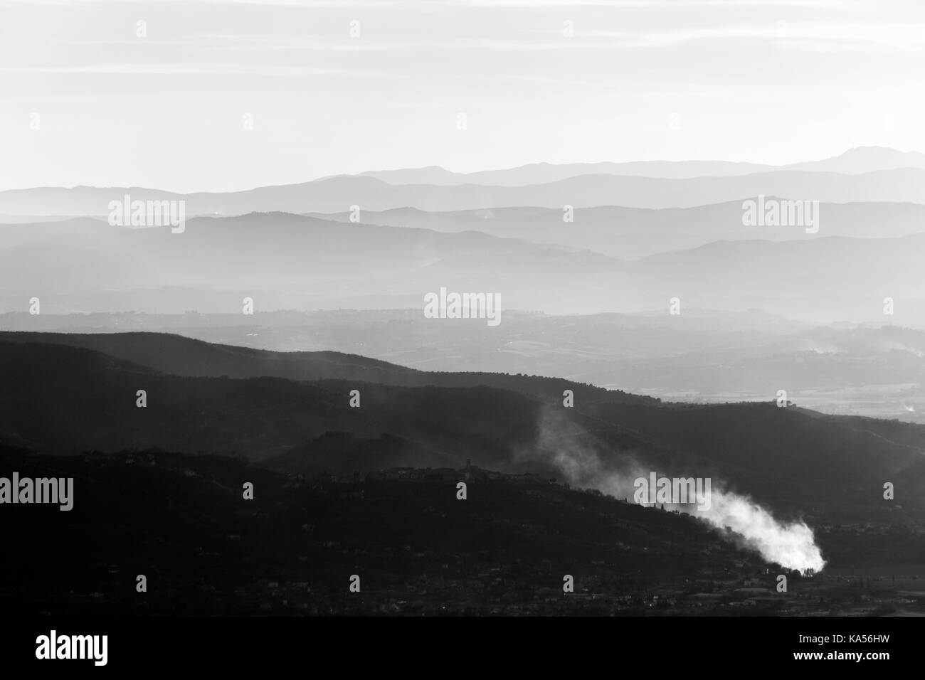 Valley filled by mist, with smoke in the foreground and distant mountains and hills in the background Stock Photo