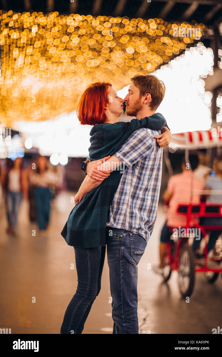 Happy couple embracing and kissing in the evening on a light garlands ...