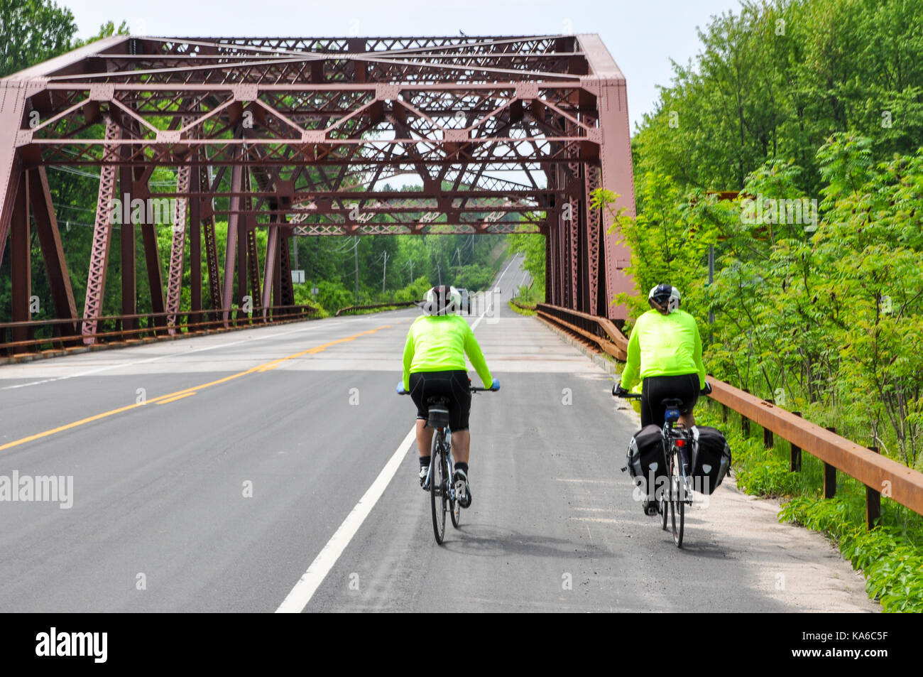 Two touring cyclists approaching a suspension bridge cycling on the Hudson Route 9 cycleway in upstate New York, USA. Stock Photo