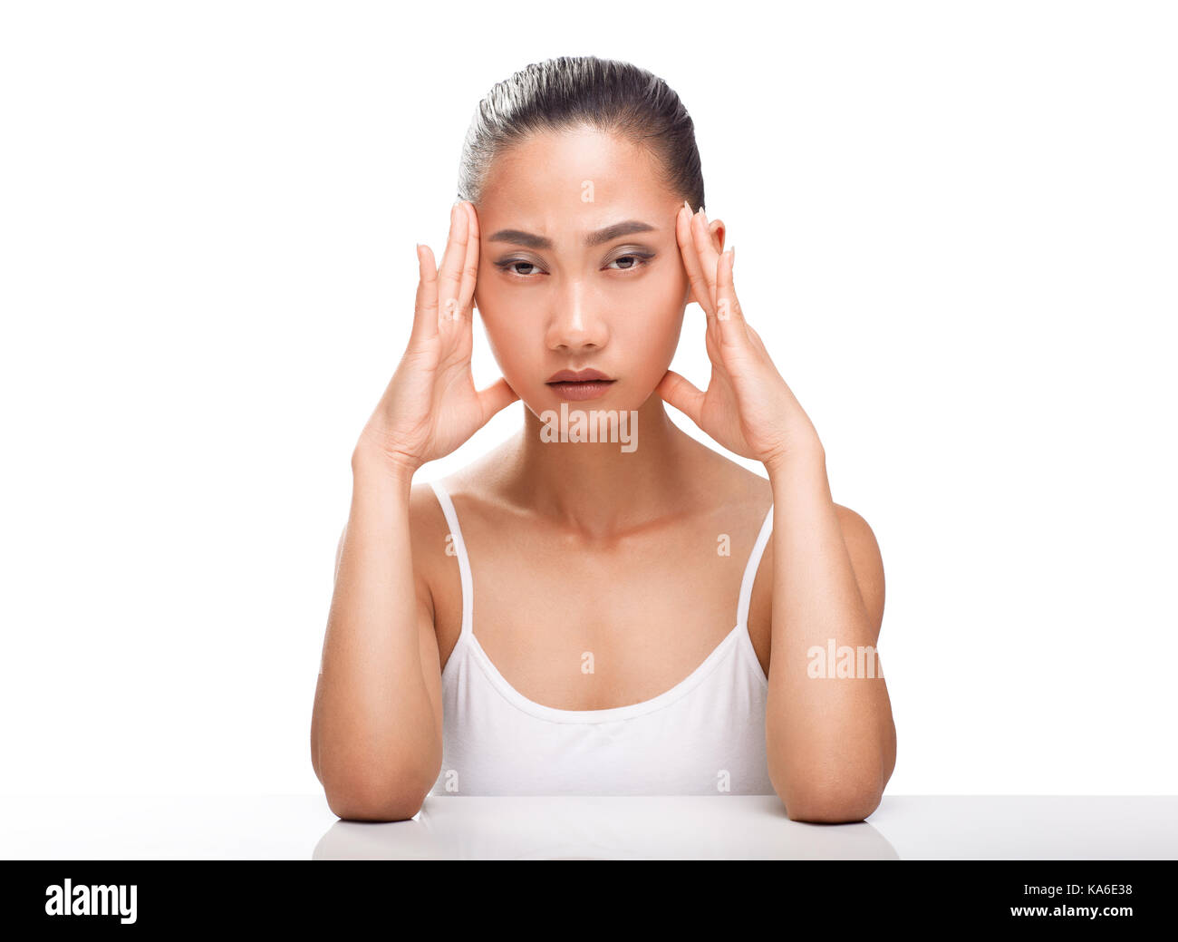 Young Asian woman having headache. Girl siting with sickly look. Expression of emotion pain, stress and fatigue. Female model isolated on white backgr Stock Photo