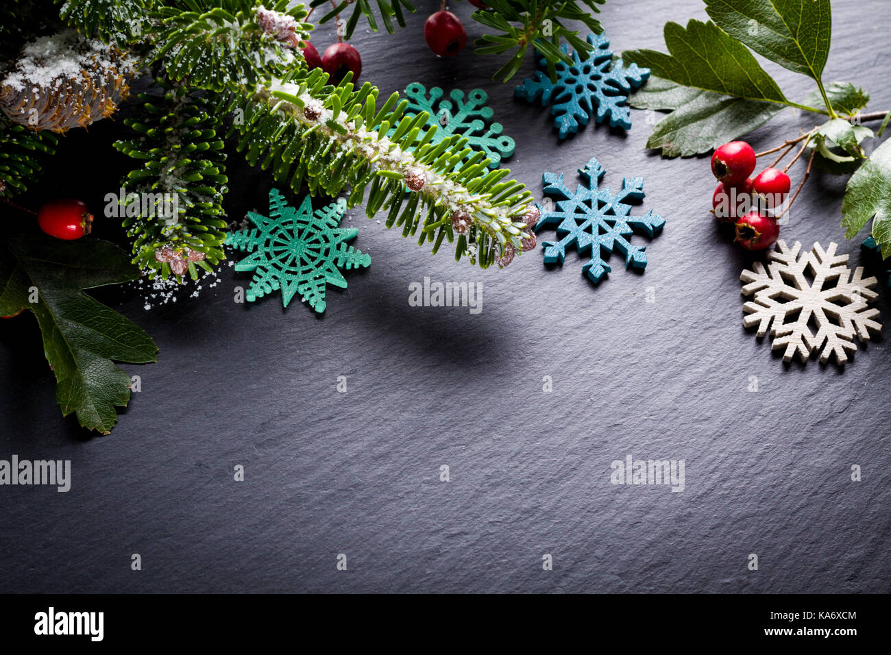Background christmas decoration twig, red berries and wooden stars on back slate. Stock Photo