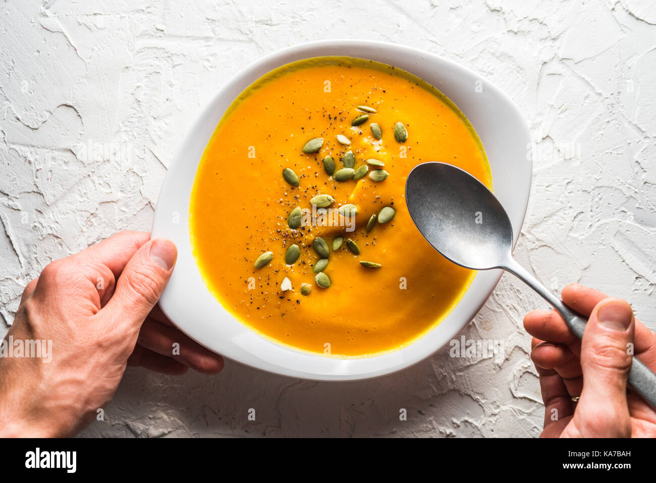 Pumpkin soup with seeds and a spoon in hand horizontal Stock Photo