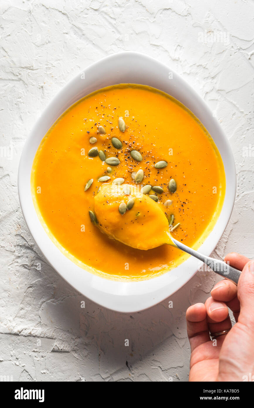 Pumpkin soup with seeds and a spoon with soup in hand vertical Stock Photo