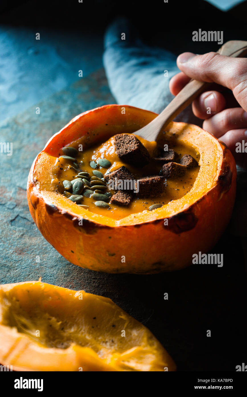 Spoon in hand with pumpkin soup and pumpkin with sunflower seeds and croutons vertical Stock Photo