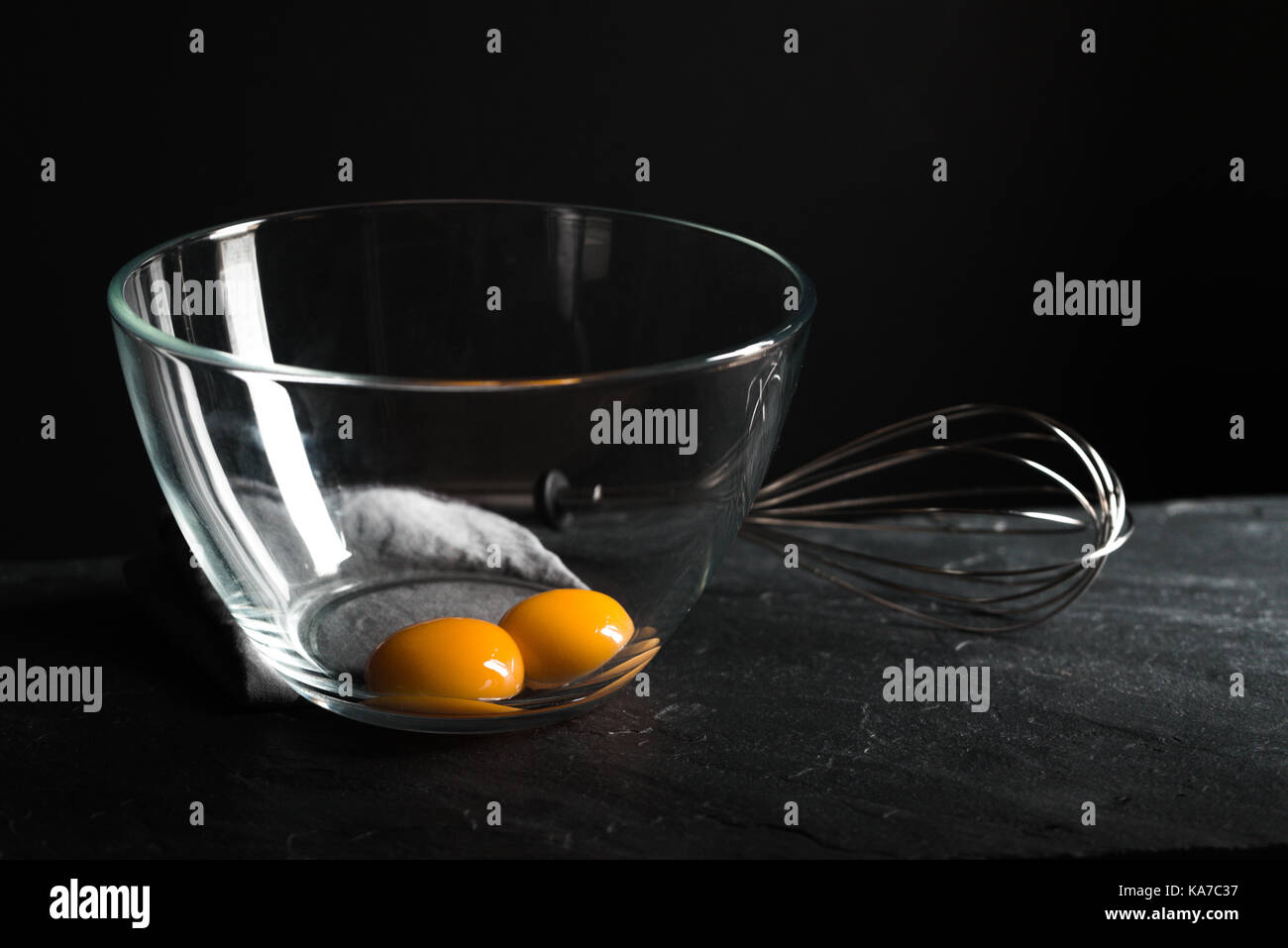 Chicken yolks in a bowl and whisk for beating on a gray table horizontal Stock Photo