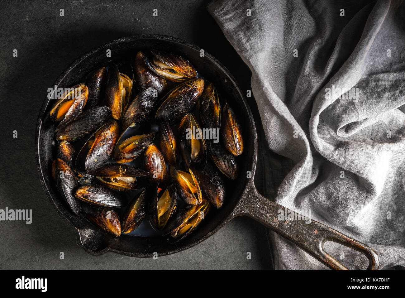 Mussels on a castiron frying pan and napkin on a gray background