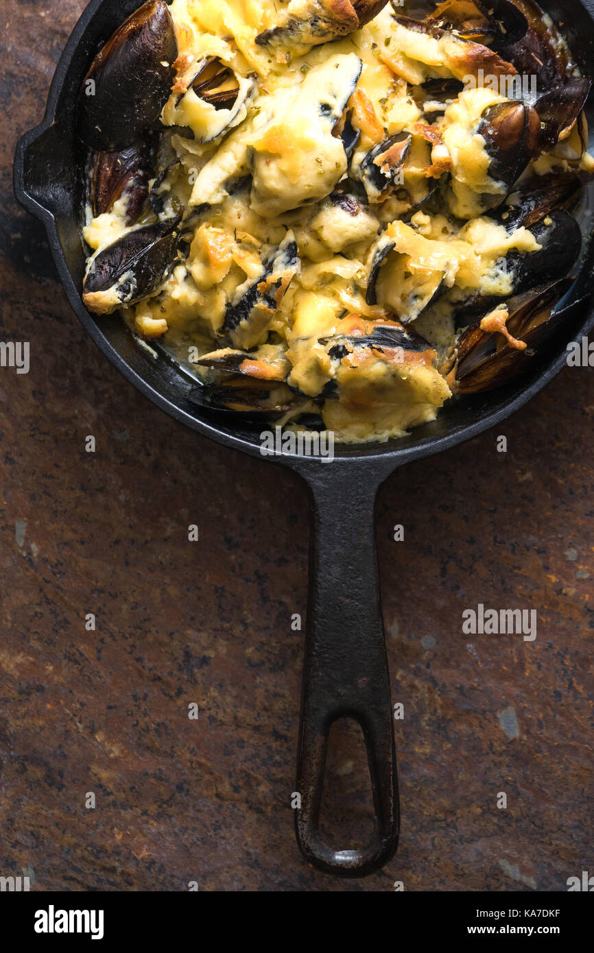 Frying pan with mussels under cheese sauce on a brown background
