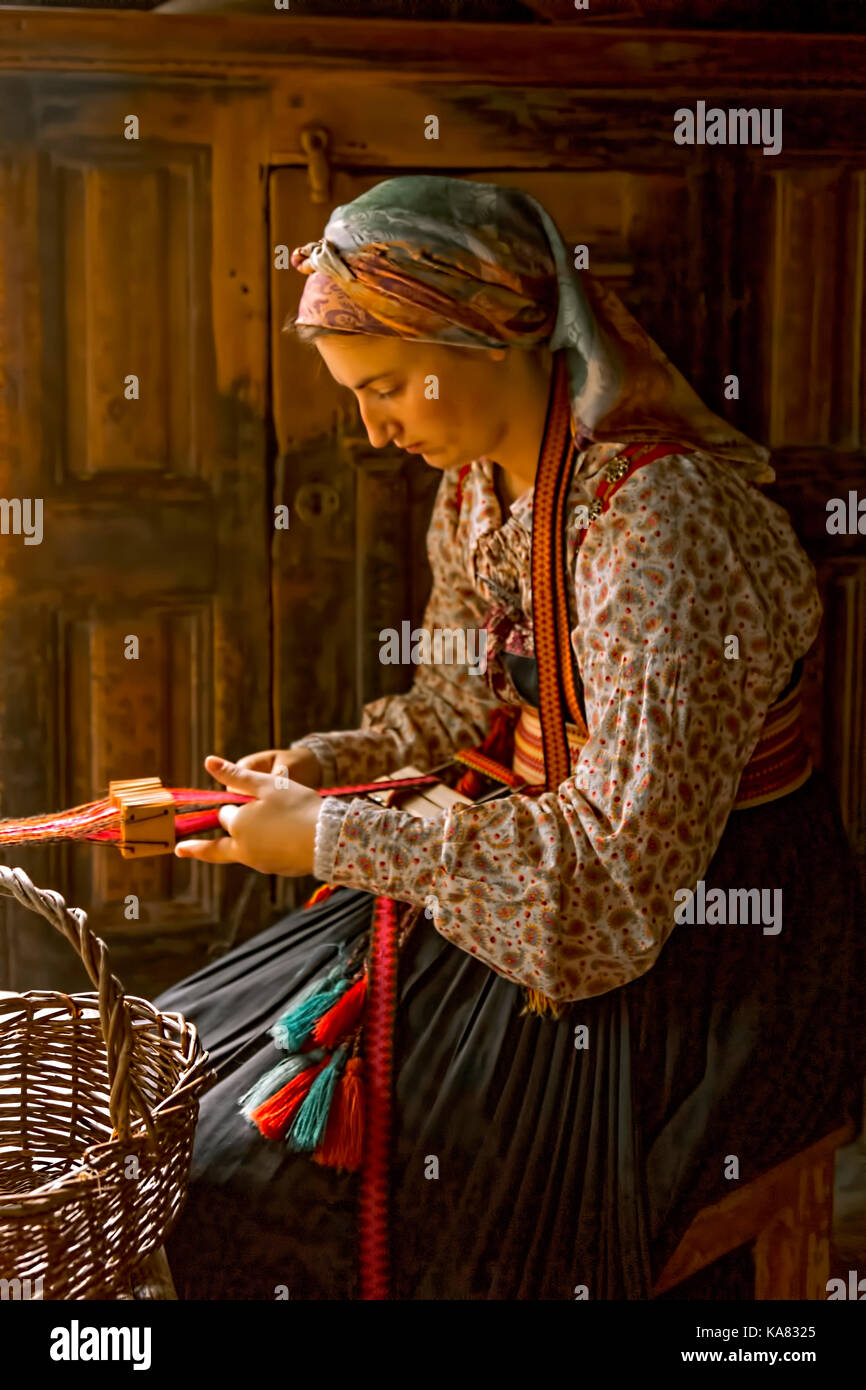 Woman in historic traditional dress acting at the NORSK FOLKEMUSEUM and concentrating on her tablet weaving, Oslo, Bygdøy, Norway. Stock Photo