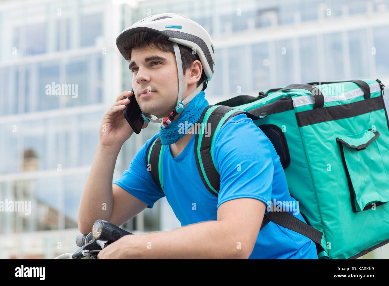 Courier On Bicycle Delivering Food In City Using Mobile Phone Stock Photo